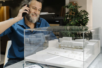 Mature man with a beard talking on the phone and looking at a model of a building. architecture concept