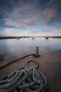 Rope and cleat on pier by sea against sky