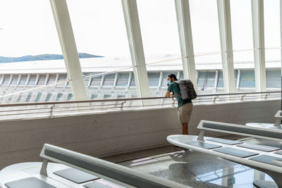 Side view of male traveler in medical mask standing in departure lounge of airport and waiting for flight during covid 19 epidemic