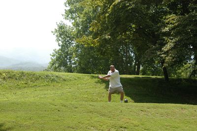 Man playing golf on grassy field against trees