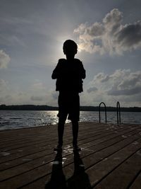 Rear view of silhouette boy standing by sea against sky