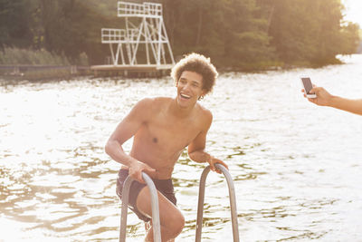 Cropped image of man photographing happy male friend coming out from lake