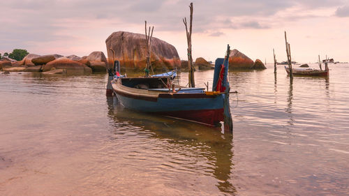 Sailboats moored on sea against sky during sunset