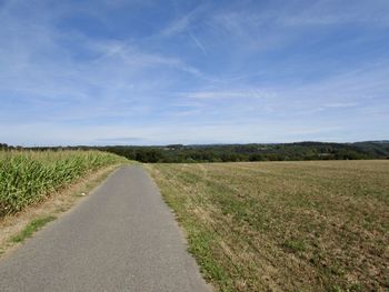 Empty road amidst field against sky