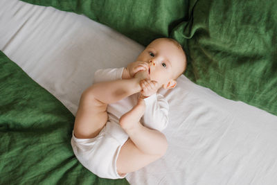 Cute baby is lying on a green and white bedspread on the bed. a smiling child having his feet