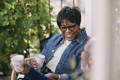 Happy senior woman wearing denim jacket enjoying drink with man