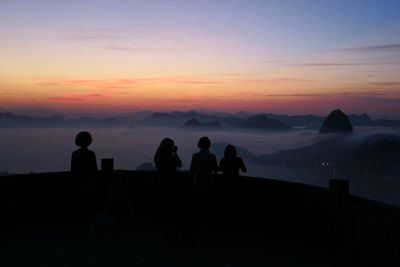 Silhouette of people standing on observation point at sunset