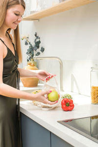 A young attractive woman takes apple out of an eco-bag in the kitchen. eco-friendly concept.