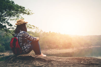 Man sitting on rock against sky during sunset