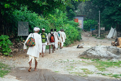 Rear view of people walking on dirt road