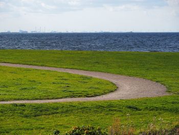 Scenic view of field by sea against sky