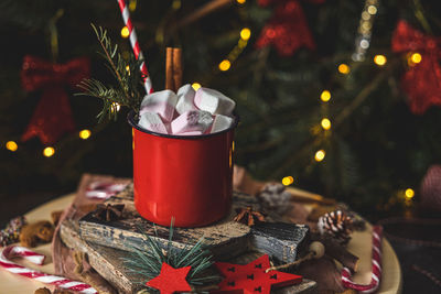 One red iron mug with hot cocoa, marshmallows from above with cinnamon, straws, spruce branch 