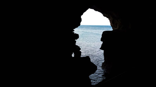 Silhouette rock formation in sea against sky