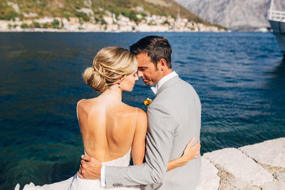 Rear view of couple embracing while sitting against sea