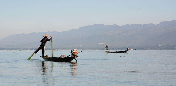 Men fishing while standing on boat in sea against mountains