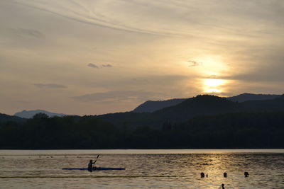 Silhouette man kayaking in lake against sky during sunset