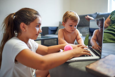 Side view of peaceful boy and girl sitting near sofa and using laptop together while choosing cartoon and resting at weekend at home