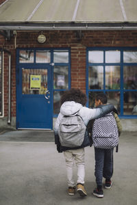 Rear view of boys with arm around walking towards school building