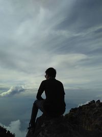 Low angle view of man sitting on rock against sky