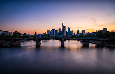 Bridge over river in city against sky during sunset