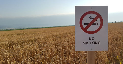 Close-up of information sign on field against sky