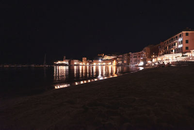 Illuminated buildings by sea against clear sky at night