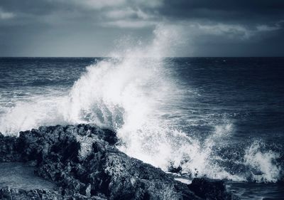 Waves splashing on rocks against sky