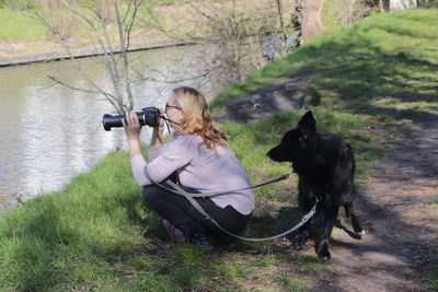 Side view of woman photographing while sitting by lake at park