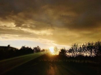 Road by silhouette trees against sky during sunset