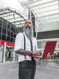 Hipster male worker in formal wear browsing netbook while standing on urban street