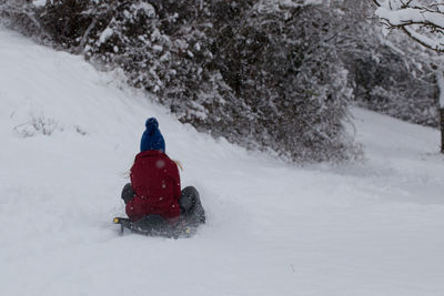 Rear view of girl sledding on snow covered field
