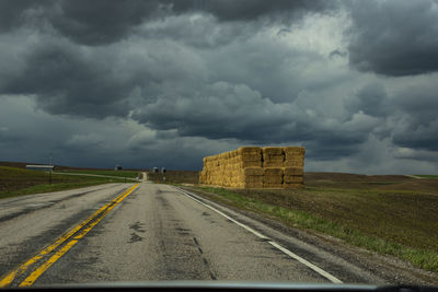 Road amidst field against storm clouds