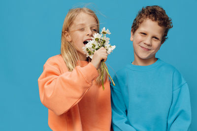 Happy siblings holding flowers while standing against blue background
