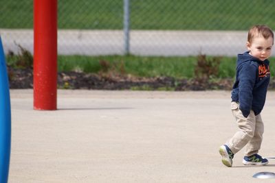 Side view of cute boy looking away while walking against fence at park