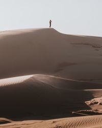 Man on sand dune in desert against sky