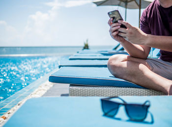 Midsection of man using mobile phone in swimming pool