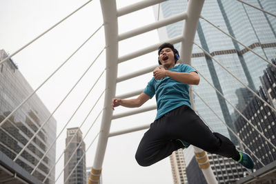 Low angle view of cheerful young man jumping while listening music against building