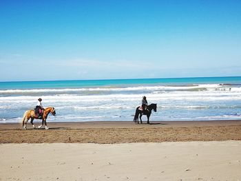 Men riding horse at beach against sky