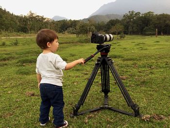 Boy standing by camera on tripod against trees