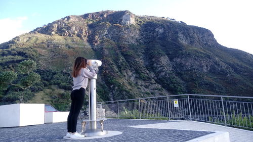 Full length of woman standing at observation point on mountain against sky