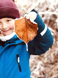 Portrait of boy holding frosted leaf while standing outdoors