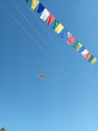 Low angle view of flags hanging against clear blue sky