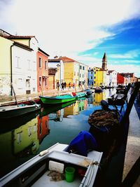 Boats moored in canal in city against sky