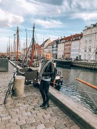 Portrait of young woman standing by river in city against sky