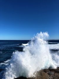 Waves splashing on sea against clear blue sky