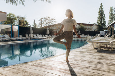 Woman standing on one leg by swimming pool