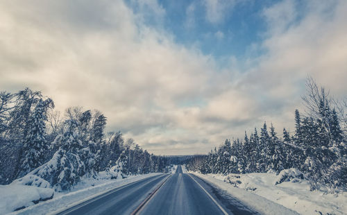 Road amidst snow covered landscape against sky