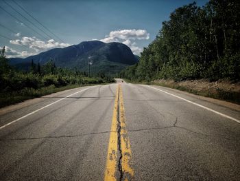 Empty road along trees and mountains against sky