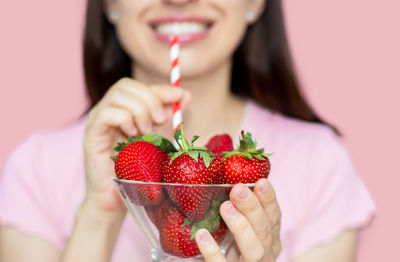 Woman bite fresh strawberry or holding in hand glass bowl with straw like milkshake vitamins smiling