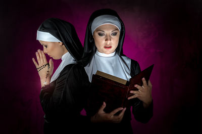 Beautiful young women reading bible and praying with rosary against illuminated black background